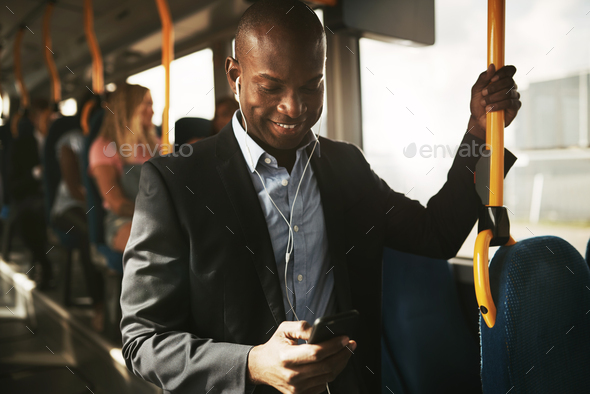 Smiling African businessman standing on a bus listening to music - Stock Photo - Images