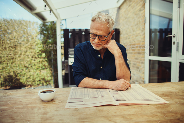 Smiling senior man enjoying a coffee and reading the newspaper - Stock Photo - Images