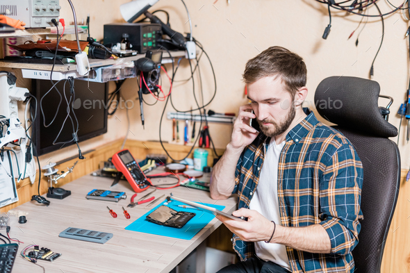 Young professional master of gadget repair service calling one of clients