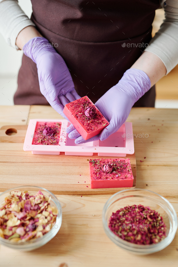Hands of young woman in lilac gloves holding bar of fresh handmade floral soap
