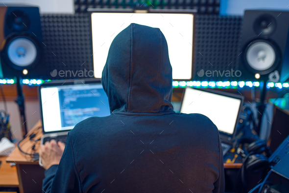Hacker in the hood sitting at laptop, back view - Stock Photo - Images