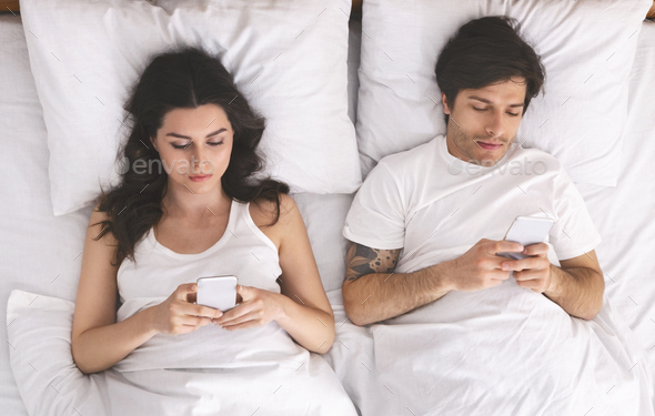 Young married couple using cellphones in bed