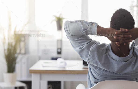 Black worker sitting in office with hands behind his head - Stock Photo - Images