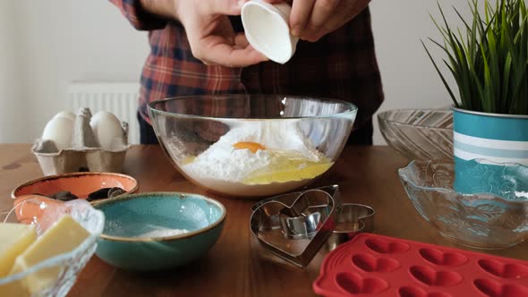 Man mixing egg and butter with flour to make cookie cakes in the kitchen.