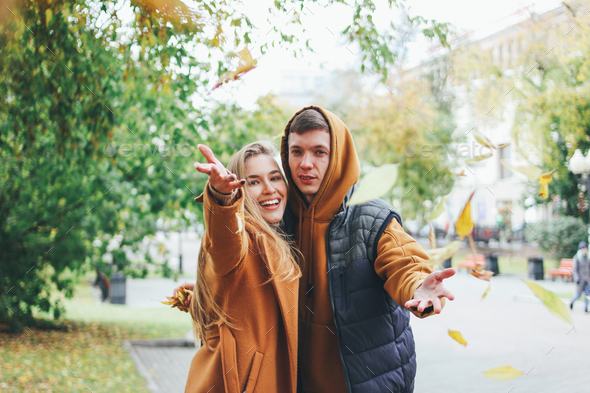 Happy young couple dressed in casual style walking and throws leaves at camera - Stock Photo - Images