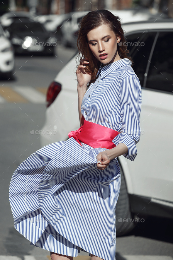 Beautiful stylish brunet girl dressed in striped white and blue dress with a bright pink belt with a