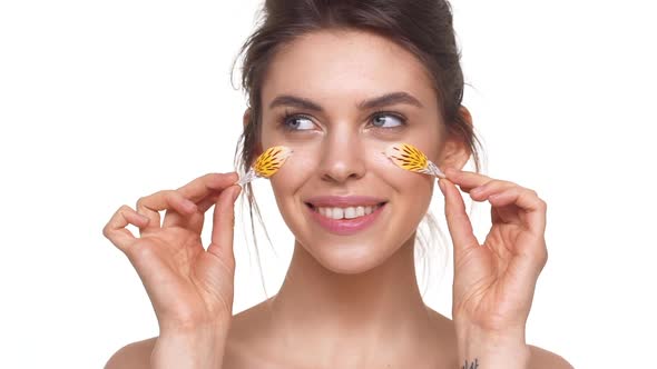 Attractive Caucasian Girl Gently Touching Face with Petals Over White Background in Slowmotion alt