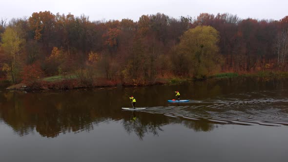 Drone Shot of Man and Woman on Sup Paddle Boards at Wide River on Golden Autumn Forest Background alt