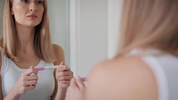 Young woman standing in front of bathroom mirror and waiting for pregnancy test results. Shot with R alt
