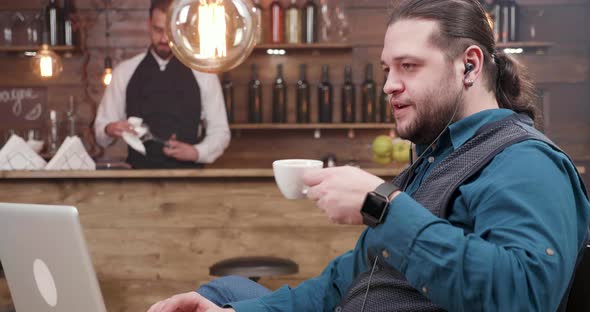 Confident Man Engaged in a Video Call Enjoys a Coffee in a Small Restaurant alt