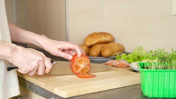 Women's hands cut tomatoes for making sandwiches on a wooden cutting board.