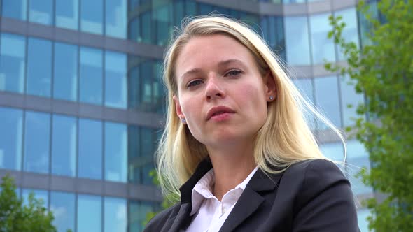A Young Beautiful Businesswoman Looks at the Camera - Closeup From Below - an Office Building alt
