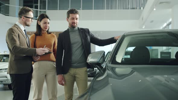 Businessman and Beautiful Wife Choosing Car in Dealership Talking To Salesman alt