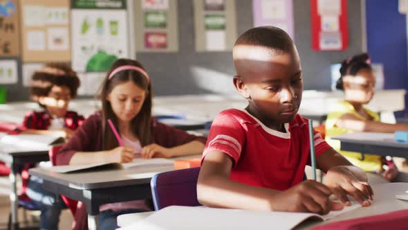 Portrait of african american schoolboy sitting in class, making notes, looking at camera alt