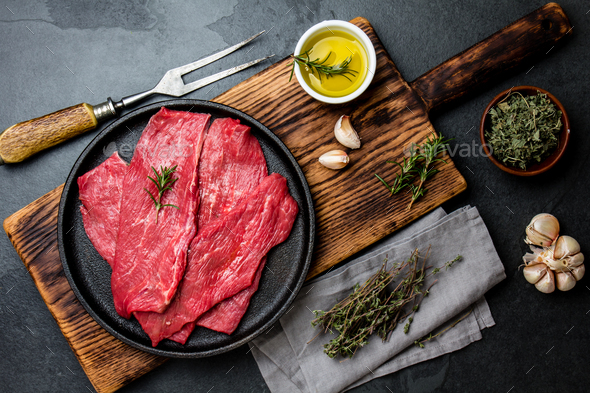 Beef tenderloin in cast iron pan on wooden board, spices, herbs, oil on slate gray background. - Stock Photo - Images