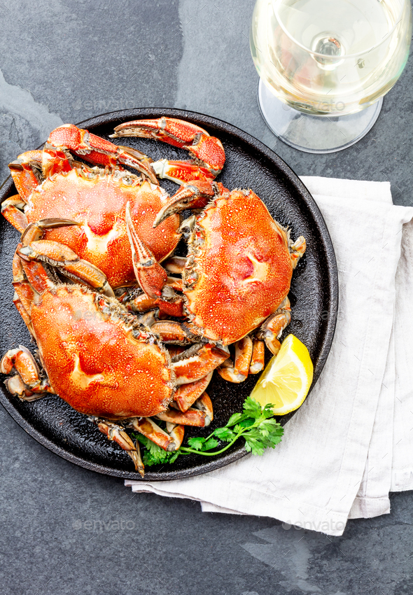 Cooked crabs on black plate served with white wine, black slate background