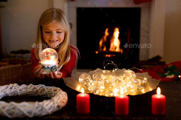 Young Caucasian girl holding a snow globe in the sitting room at Christmas time, smiling