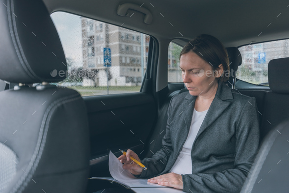 Businesswoman doing business paperwork on car back seat