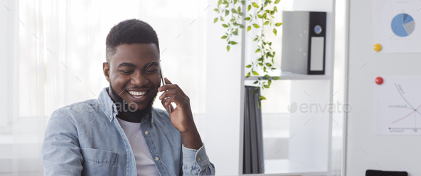 Happy black employee talking on cellphone at worplace in office