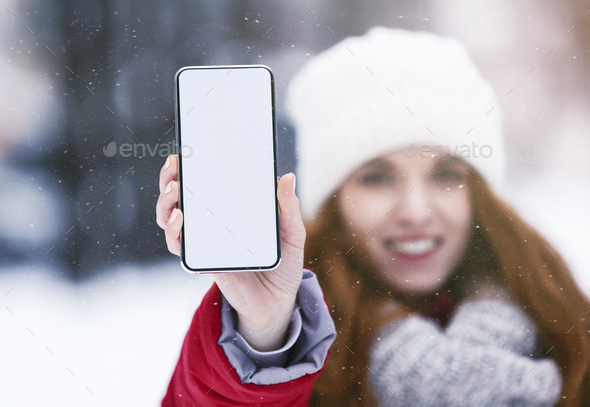 Girl showing blank smartphone screen in snowy park