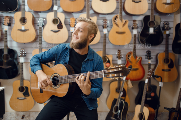 Young man plays on acoustic guitar in music store