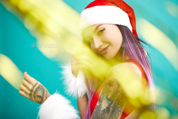 Charming girl with purple hair tips and tattoo on her arm dressed in red swimsuit, Santa's hat