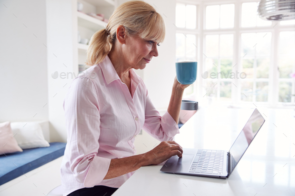 Mature Disabled Woman With Crutches At Home Working On Laptop On Kitchen Counter
