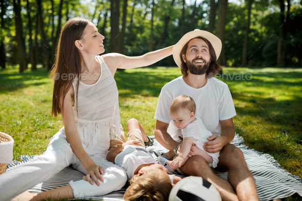Warm sunny day in the park. Stylish young family dressed in white casual clothes is sitting on a - Stock Photo - Images