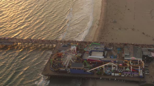 AERIAL: Flying Away From Santa Monica Pier, Los Angeles at Beautiful Sunset with Tourists alt