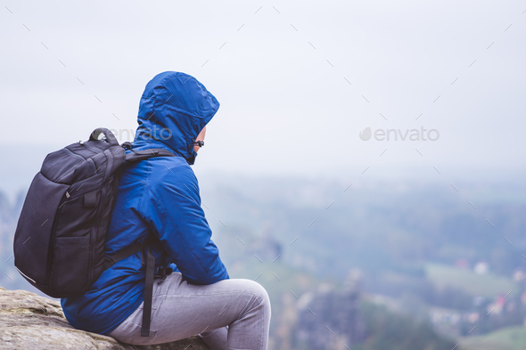 Lonely hiker wear outdoor clothing with backpack sitting on mountain edge, enjoying view of - Stock Photo - Images