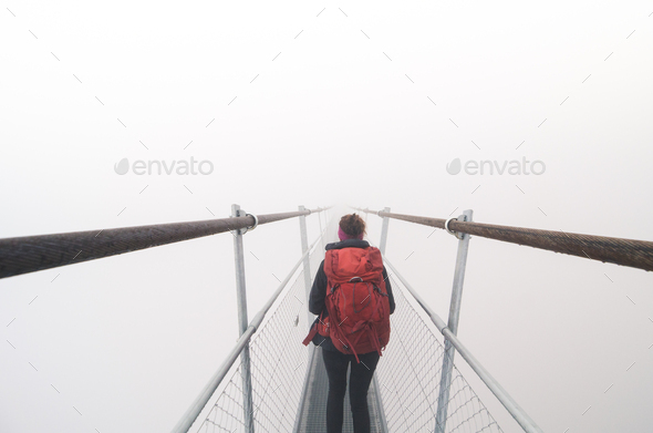 Female tourist walking across a suspension bridge in heavy fog - Stock Photo - Images