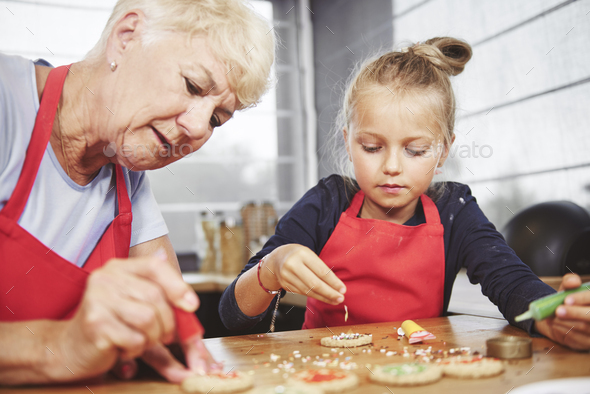 Grandma with girl applying icing on cookies
