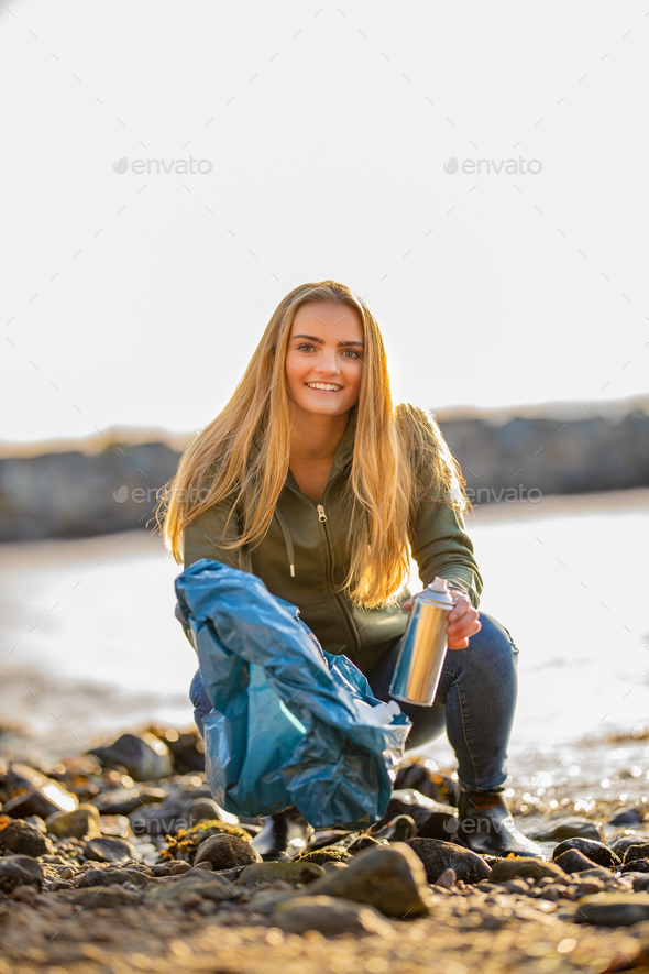 Young woman picking up aerosol can at beach - Stock Photo - Images