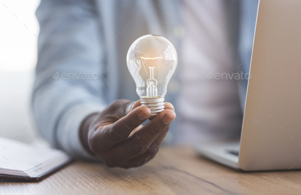 Black businessman holding illuminated light bulb in hand - Stock Photo - Images