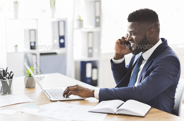 Cheerful young entrepreneur having conversation with business partner by cellphone