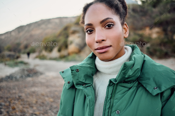 Beautiful casual African American girl in down jacket dreamily looking in camera walking outdoor
