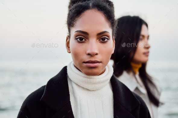 Beautiful casual African American girl intently looking in camera walking with friend by the sea