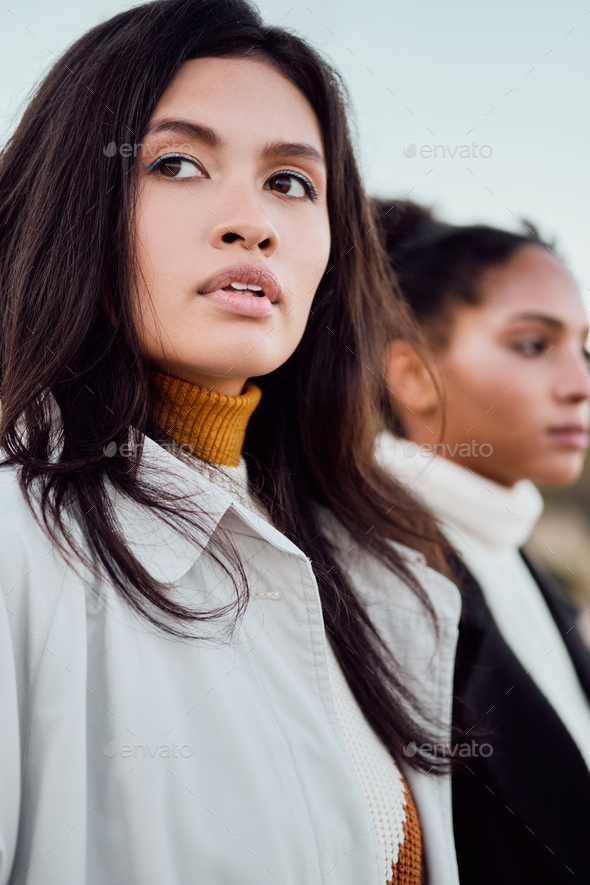 Beautiful Asian girl thoughtfully looking away standing with African American friend by the sea
