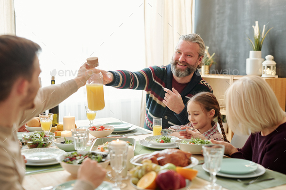Happy senior man passing bottle of orange juice to his son over served table - Stock Photo - Images