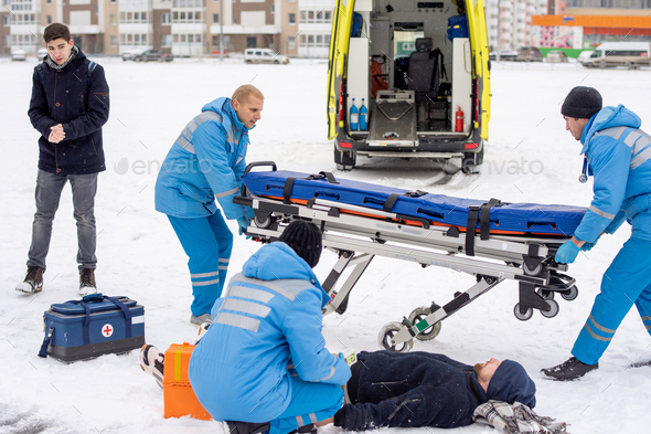 Brigade of young paramedics in workwear preparing stretcher for unconscious man