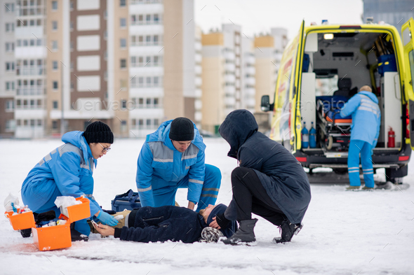 Two paramedics in uniform and guy giving first aid to sick unconscious man
