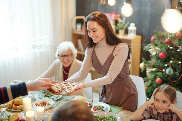 Happy young woman giving homemade pie to her father over served festive table