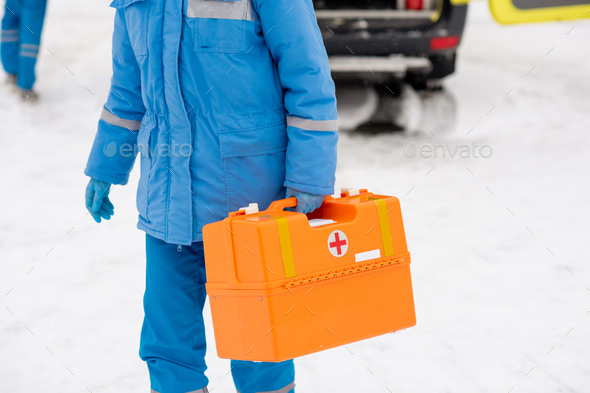 Young paramedic in workwear carrying first aid kit while going to sick person