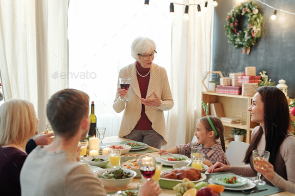 Senior grey-haired woman with glass of red wine pronouncing Thanksgiving toast