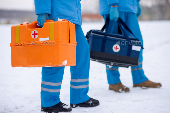 Low section of two paramedics in uniform and gloves carrying first aid kits