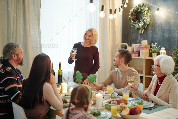 Happy mature female with glass of wine making festive toast by served table