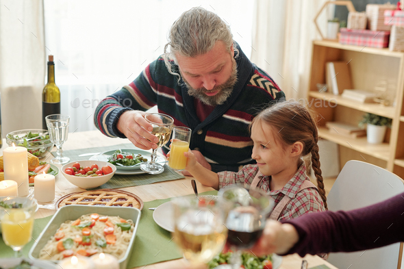 Senior man with glass of wine toasting with his granddaughter over served table