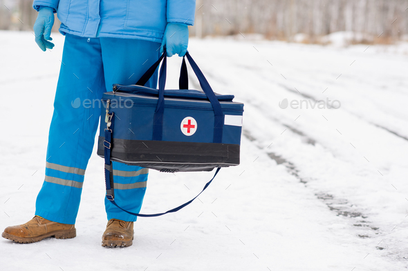 Young paramedic in blue workwear holding first aid kit with red cross