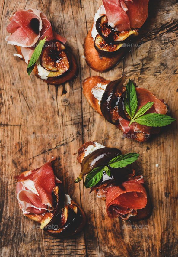 Crostini with prosciutto, cheese and figs on rustic wooden board - Stock Photo - Images