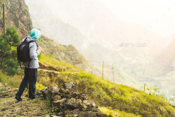 Traveler with backpack staying on the edge of path leading through rural landscape with mountains - Stock Photo - Images
